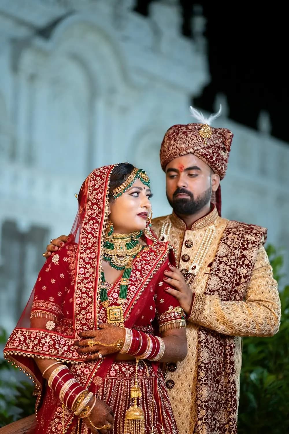 Bride and groom in red and gold before a white palace wall